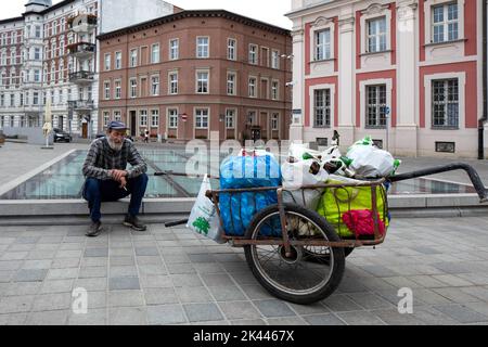 Poznan, Polen - Ein Mann, der Flaschen für seinen Lebensunterhalt sammelt und auf einer Wand auf dem Kolegiacki-Platz sitzt. Stockfoto