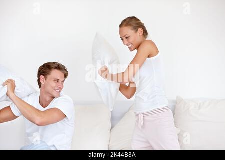 Ein paar gute Laune. Ein junges Paar trägt Pjamas und kämpft gemeinsam mit einem Kissen. Stockfoto