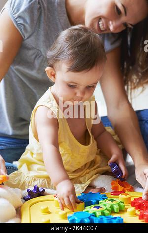 Shes so ein cleveres kleines Mädchen. Ein entzückendes Mädchen sitzt auf dem Boden mit ihrer Mutter und spielt mit Spielzeug. Stockfoto