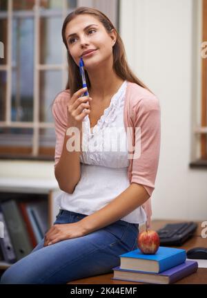 Denken Sie an ihre nächste Klasse. Eine schöne junge Lehrerin, die in ihrem Büro sitzt. Stockfoto