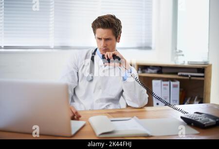 Ein junger Arzt sitzt in seinem Büro und telefoniert. Stockfoto
