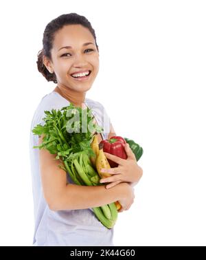 Ausgestattet mit den frischesten Zutaten. Junge Frau lächelt, während sie eine Armvoll frisches Gemüse hält - isoliert. Stockfoto