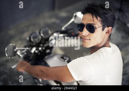 Es ist nur uns und die Straße. Ein hübscher junger Mann, der auf seinem Motorrad sitzt. Stockfoto