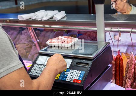 Metzger, der ein Tablett mit Würstchen auf einer Waage wiegt. Vertriebskonzept. Stockfoto