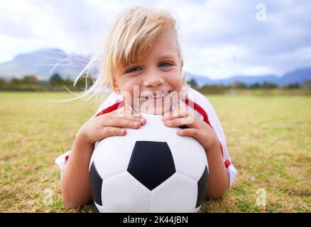 Sie liebt das Spiel. Ein junger Fußballspieler, der auf dem Gras liegt, während er einen Ball hält. Stockfoto