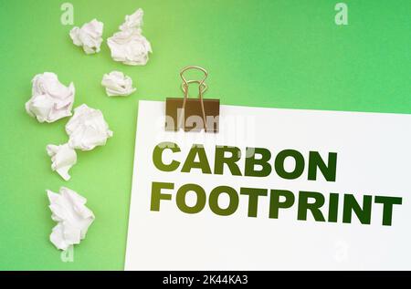 Ökologisches Konzept. Auf grünem Hintergrund zerknittertes Papier und ein Blatt mit der Aufschrift - Carbon Footprint Stockfoto