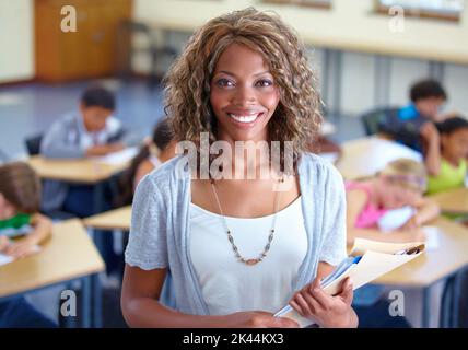 Anreichern eifriger junger Köpfe. Porträt einer glücklichen jungen Lehrerin mit ihren Schülern im Hintergrund. Stockfoto