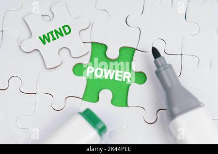 Ökologisches Konzept. Weiße Rätsel liegen auf einem grünen Hintergrund, anstelle eines offenen Puzzles steht geschrieben - Wind Power Stockfoto