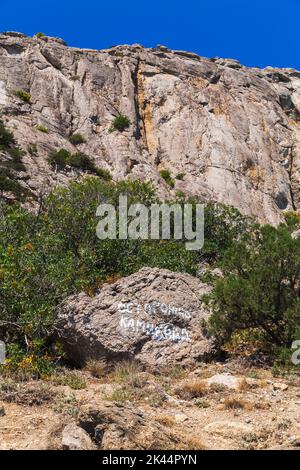 Sommer Krimlandschaft mit russischem Text auf einem Stein: Vorsicht, Steinschlag. Felsige Berge liegen auf einem Hintergrund Stockfoto