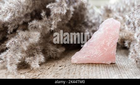 Rosenquarz-Mineralexemplar auf Holzhintergrund. Rosenquarz ist ein heilender rosafarbener Stein, der die Liebe einatert und Gefühle fördert Stockfoto