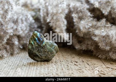 Nahaufnahme von grobem, ungeschnittenem Labradorit-Edelstein in Felsform auf Holzgrund. Bunte Blitze von Labradorit auf Felsen Stockfoto