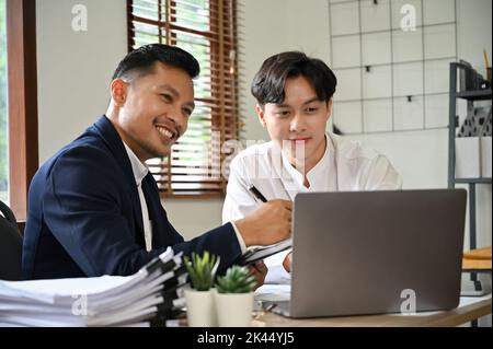 Professionelle und intelligente asiatische männliche Finanzberater analysieren die Finanzdaten des Berichts, betrachten den Laptop-Bildschirm, treffen sich und arbeiten zusammen Stockfoto