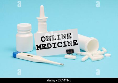 Medizinkonzept. Auf blauem Hintergrund ein Thermometer, Pillen und eine Visitenkarte mit der Aufschrift - Online Medicine Stockfoto