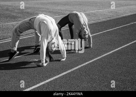 Flexible Mädchen Turnerinnen stehen in Krabbenposition auf der Leichtathletik-Strecke, Flexibilität Stockfoto