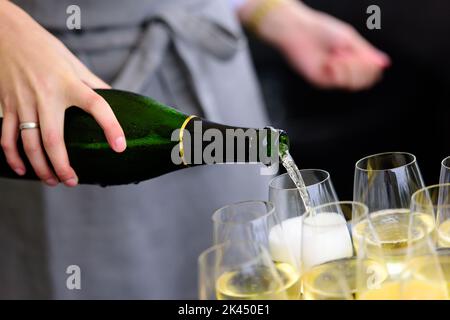 Nahaufnahme einer Champagnerflasche, die Champagner auf einer Sektflöte gegen eine verschwommene Person auf einer Party umschaufelt Stockfoto