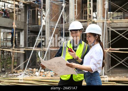 Architektin und Bauarbeiter-Manager im Schutzhelm besprechen auf der Baustelle die Plandetails Stockfoto