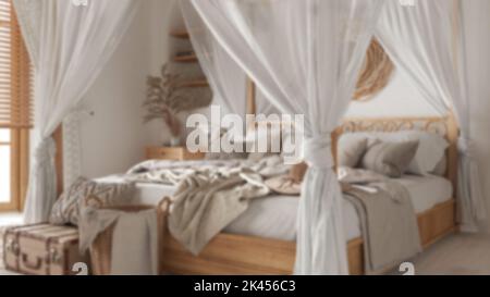 Verschwommener Hintergrund, Nahaufnahme des Schlafzimmers mit Himmelbett. Decken, Bettdecken und Kissen. Böhmische Rattan- und Holzmöbel. Innenarchitektur im Boho-Stil Stockfoto