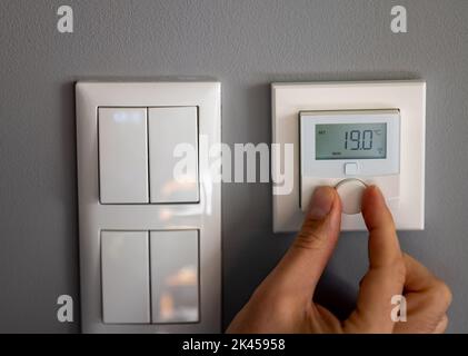 Hand dreht die Temperatur auf 19 Grad Celsius auf einem elektronischen Thermostat. Symbol für Energieeinsparung. Stockfoto