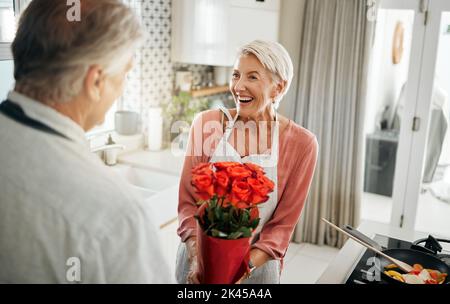 Blumen, Liebe und Kochen mit einem älteren Paar in einer Küche für ein Überraschungsfrühstück zur Feier eines Jubiläums, Geburtstags oder Valentinstag. Essen Stockfoto