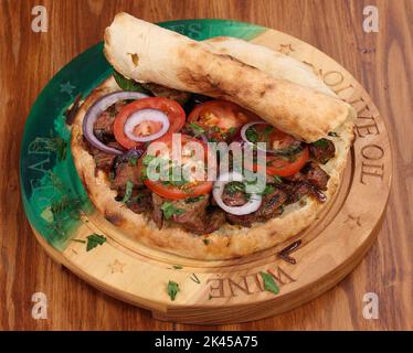 Rolle gefüllt mit Shish Kebab mit Tomaten, Kräutern, Ketchup und Amyonnaise auf einem Holztisch Stockfoto