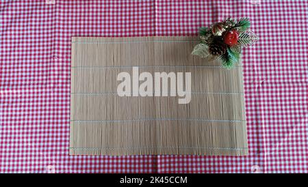 Weihnachtlich dekorierter Tisch mit leerem Etikett. Struktur des Tischsets aus Bambusrohr direkt über Ansicht, Nahaufnahme. Stockfoto