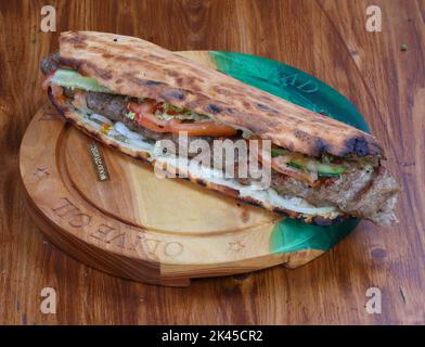 Rolle gefüllt mit Shish Kebab mit Tomaten, Kräutern, Ketchup und Amyonnaise auf einem Holztisch Stockfoto