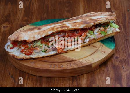 Rolle gefüllt mit Shish Kebab mit Tomaten, Kräutern, Ketchup und Amyonnaise auf einem Holztisch Stockfoto