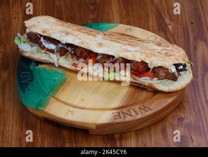 Rolle gefüllt mit Shish Kebab mit Tomaten, Kräutern, Ketchup und Amyonnaise auf einem Holztisch Stockfoto