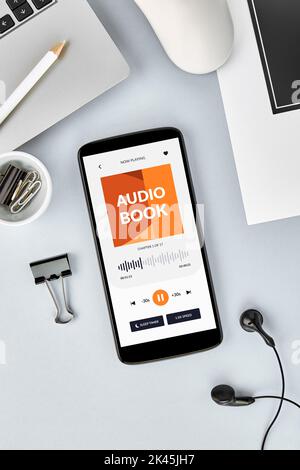 Vertikale Ansicht des Smartphone-Bildschirms von oben mit geöffneter Hörbuch-App auf dem Schreibtisch. Stockfoto