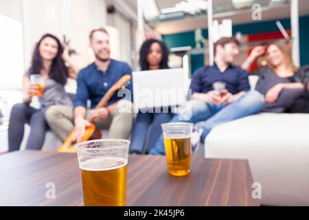 Gruppe von Freunden mit Spaß trinken Bier und Gitarre spielen auf der Couch. Verschwommenes Bild Stockfoto