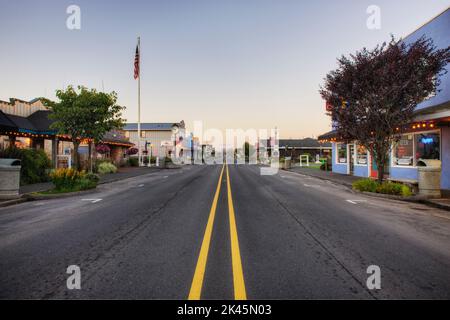 Straße auf der Hauptstraße, die im Morgengrauen durch eine leere Stadt führt. Stockfoto