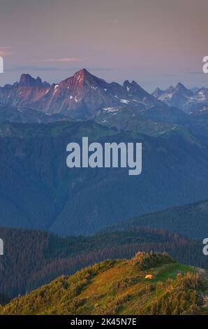 Blick von oben, ein kleines orangefarbenes Zelt, das auf einem Bergrücken aufgeschlagen ist, mit Blick auf das Tal und die Bergkette dahinter. Stockfoto