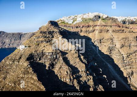 Luftaufnahme einer Stadt auf der Spitze einer steilen Klippe auf der Insel Egeo und der gewundene Weg zu einem Haus unten, an den steilen Hängen. Stockfoto