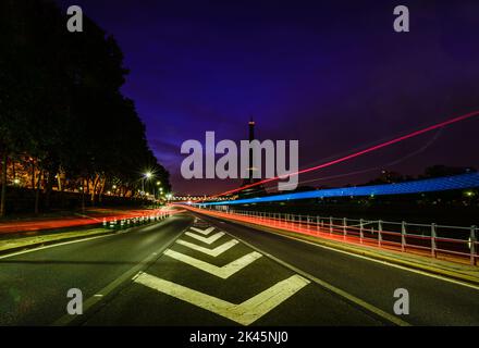 Ein Blick entlang einer Stadtstraße bei Nacht, hohe Gebäude und leichte Wege, der Eiffelturm in der Ferne. Stockfoto