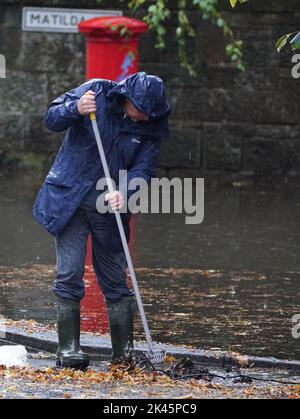 Ein Mann versucht, die Überschwemmungen zu lindern, indem er herbstliche Trümmer aus den Abflüssen während starker Regenfälle in Glasgow entfernt. Bilddatum: Freitag, 30. September 2022. Stockfoto