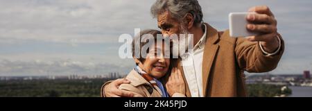 Bärtiger älterer Mann, der den Kopf einer fröhlichen Frau küsst und Selfie, Banner, Stockbild macht Stockfoto