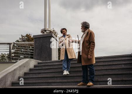 In voller Länge von stilvollen Senior Mann in Mantel zu Fuß auf Treppen und die Hand der glücklichen Frau, Stockbild Stockfoto