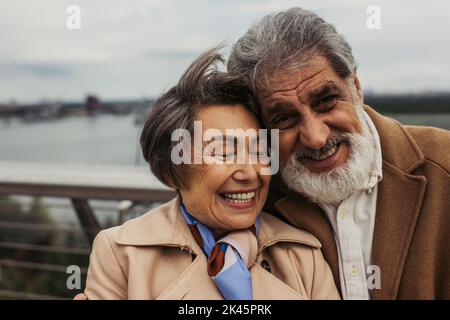 Porträt eines glücklichen älteren Paares in beigen Mänteln, lächelnd, Stockbild Stockfoto