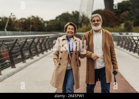 Fröhliche ältere Frau, die mit einem glücklichen Mann auf der Brücke den Regenschirm hält, Stockbild Stockfoto