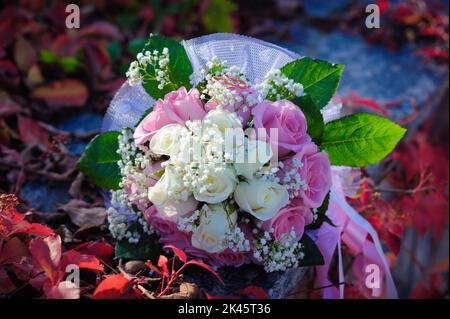 Brauthochzeit Blumenstrauß mit goldenen Ringen. Hochzeitsstrauß aus rosa und weißen Rosen, der auf einem Gras liegt Stockfoto