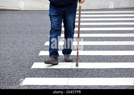 Mann, der mit einem Stock auf dem Fußgängerweg läuft. Männliche Beine bei Fußgängerübergängen, Straßensicherheit Stockfoto