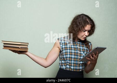 Buch und digitales Tablet. Eine Frau hat die Wahl zwischen Büchern in der einen Hand und einem digitalen Tablet in der anderen Stockfoto