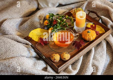 Tasse Tee, bunte Herbstblätter, Dekoration und eine Kerze auf einem Holztablett auf einer warmen Wolldecke auf dem Sofa serviert, gemütliche Herbstzeit, Kopie sp Stockfoto