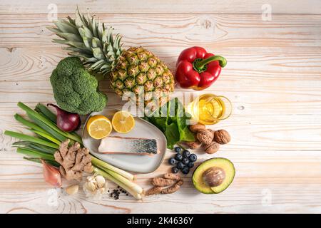 Entzündungshemmende Lebensmittel, Zutaten, frisches Gemüse, Fisch, Obst, Nüsse und Gewürze für eine gesundheitsfördernde Ernährung auf hellem Holzhintergrund, Stockfoto