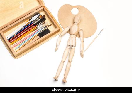 Künstlerische Pinsel und eine Spachtel in einer Schachtel und eine Holzfigur auf weißem Hintergrund Stockfoto