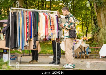 Lviv, Ukraine - September 29. 2022 : junger Hipster-Mann beim Einkaufen auf dem Flohmarkt. Kleidung an Kleiderbügeln - Second Hand Bekleidungsgeschäft oder Sparsamkeit Shopping Konz Stockfoto