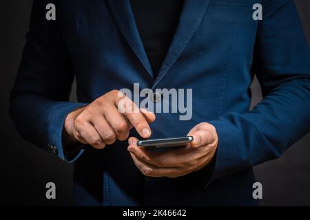 Geschäftsmann in Suit verwaltet Geschäftsprozesse mithilfe von Mobiltelefonen auf dunklem Hintergrund. Ausgeschnittene Aufnahme eines Mannes mit Mobiltelefon im Dunkeln. Mann Hand Hol Stockfoto