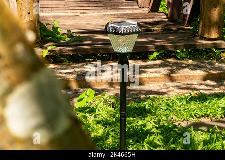 Blick auf die LED-Beleuchtung Solarlampe, die tagsüber an einer kleinen Holzbrücke in der Nähe von Granitplatten-Pfad in einem grünen Garten eingeschaltet wird. Stockfoto