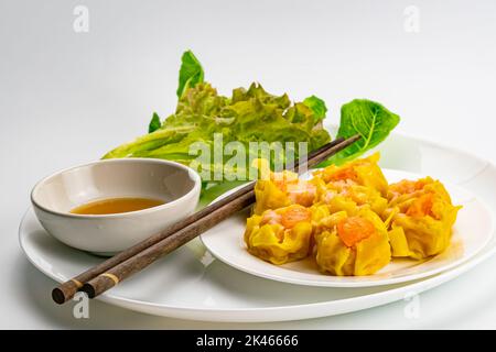 Frische leckere hausgemachte Garnelen, Hackfleisch und gesalzenes Eigelb gedünstete Knödel in weißer Keramikschale mit Sauce in weißer Keramikschale, frisches Grün Stockfoto