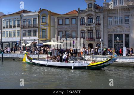 Aveiro, Portugal - 14. August 2022: Touristen steigen aus und stehen Schlange, um eine festgetäute Gondel mit Gebäuden im Kolonialstil im Hintergrund zu besteigen Stockfoto